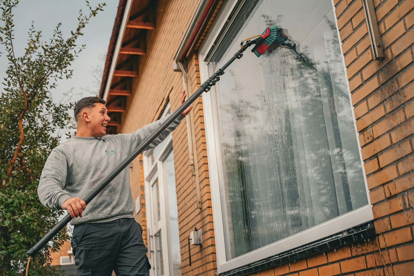 Window cleaner washing a second-floor window with a water-fed pole